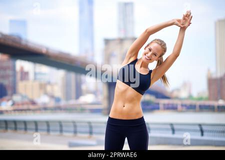 Eine Dehnung. Porträt einer schönen Frau, die sich vor ihrem Lauf in der Stadt ausdehnt. Stockfoto