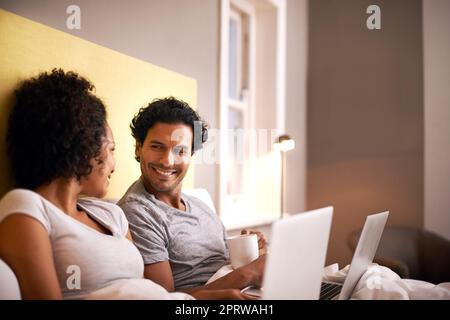 Sie schlägt mich bei diesem Spiel immer wieder. Ein junges Paar im Bett mit ihren Laptops. Stockfoto