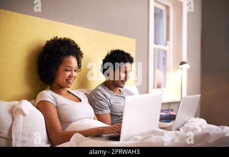 Nur noch eine E-Mail ... Ein junges Paar im Bett mit ihren Laptops. Stockfoto
