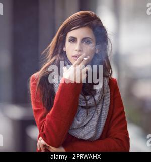 Wenn das Verlangen ruft. Porträt einer schönen und modischen jungen Frau, die in einer städtischen Umgebung eine Zigarette raucht. Stockfoto