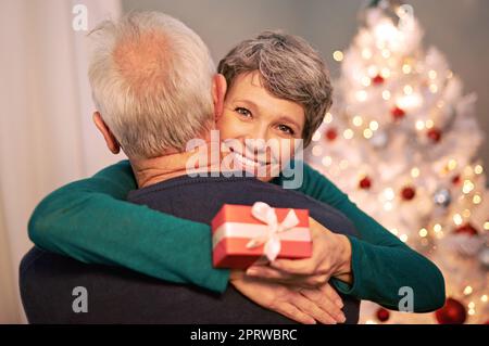 Mein eigener Weihnachtsmann. Porträt einer glücklichen reifen Frau, die ihren Mann umarmt, nachdem sie ein Weihnachtsgeschenk von ihm erhalten hat. Stockfoto