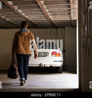 Auf dem Weg zur Absetzung. Rückansicht eines Mannes, der in einer Garage auf sein geparktes Auto zuläuft. Stockfoto