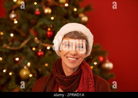 Ein fröhliches Weihnachten für alle. Ein verkürztes Porträt einer glücklichen reifen Frau mit weihnachtsmann-Hut. Stockfoto