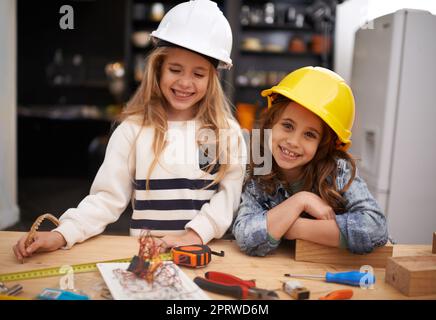 Angehende kleine Erfinder. Zwei kleine Mädchen in Hüten, die zu Hause mit Werkzeugen spielen. Stockfoto