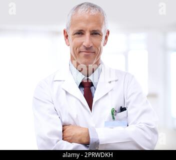 Ihre Gesundheit ist meine oberste Priorität. Porträt eines reifen Arztes, der mit gekreuzten Armen steht. Stockfoto