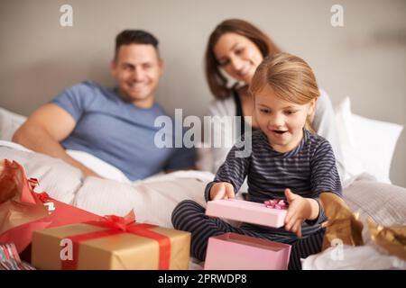 Die große Eröffnung. Ein kleines Mädchen erhält Geschenke im Bett von ihren Eltern. Stockfoto