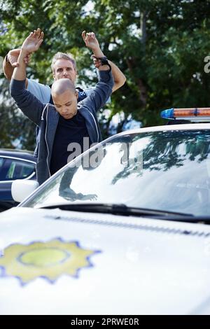 Lege deine Hände in die Luft. Ein Mann steht mit seinen Händen in der Luft, während ein Polizist ihn festhält. Stockfoto