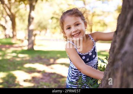 Du wirst mich nie fangen. Porträt eines kleinen Mädchens, das im Park versteckt und gesucht wird. Stockfoto