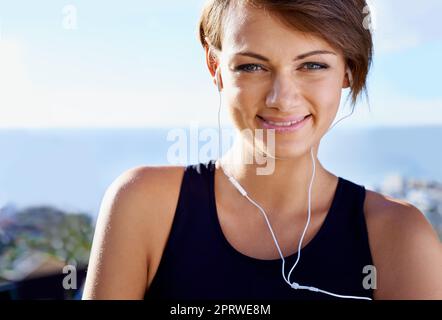 Sie genießt ihre morgendlichen Workouts. Eine sportliche junge Frau, die draußen Musik hört. Stockfoto