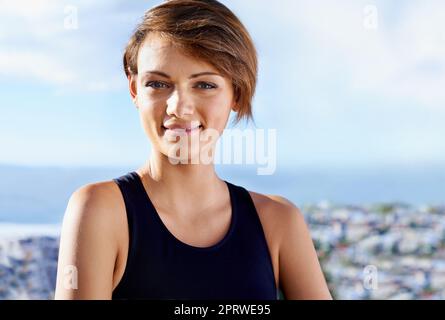 Genießen Sie ein Workout an der frischen Luft. Eine lächelnde junge Frau in Übungskleidung, die draußen steht. Stockfoto