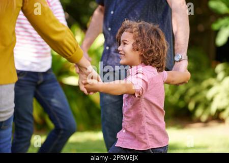 Ein kleiner Junge, der mit seiner Familie im Garten eine Partie Ring-a-Rosy genießt. Stockfoto