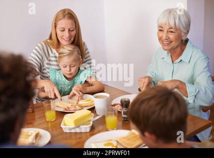 Mütter sind ein Experte für Multitasking. Eine kurze Aufnahme einer glücklichen Familie aus mehreren Generationen, die zu Hause zusammen frühstücken kann. Stockfoto