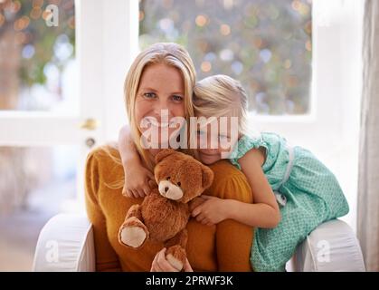 Mama, Teddy und ich. Beschnittenes Porträt eines kleinen Mädchens, das mit ihrer Mutter und ihrem Teddybär sitzt. Stockfoto