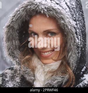 Liebe den ersten Schneefall. Eine attraktive Frau, die sich draußen im Schnee genießt. Stockfoto