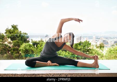 Beginnen Sie den Tag mit einem Stretching-Workout. Ganzkörperaufnahme einer sportlichen jungen Frau, die sich auf einer Trainingsmatte dehnt. Stockfoto