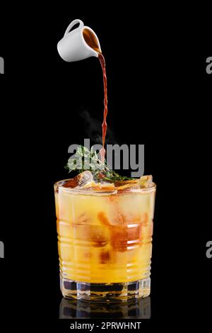 Gießen Sie heißen Espresso in ein Glas mit Tonic- und Orangensirup und Thymian Stockfoto