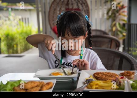 Kleine asiatische Mädchen essen Spiegelei auf Gericht am Tisch. Stockfoto