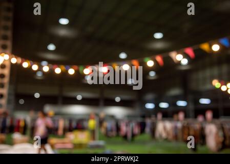 Verschwommenes Bild von Menschen auf dem Nachtmarkt, die auf der Straße spazieren, mit einem hellen Bokeh im Hintergrund. Stockfoto