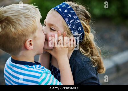 Sie haben keine Angst, ein wenig Zuneigung zu zeigen. Ein kleines Mädchen, das ihrem Bruder einen Kuss gibt, während sie draußen zusammen spielen Stockfoto