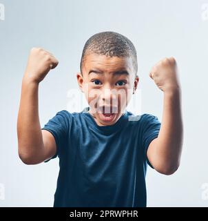 Aufwachsen mit einem starken Selbstwertgefühl. Studioaufnahme eines niedlichen kleinen Jungen, der seine Muskeln vor einem grauen Hintergrund beugend. Stockfoto