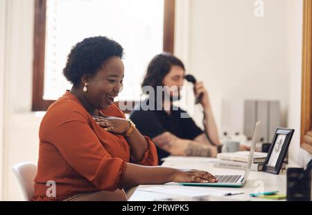 Es sieht so aus, als wäre heute Glück auf meiner Seite. Eine junge Geschäftsfrau, die überrascht aussieht, als sie in einem Büro an einem Laptop arbeitet. Stockfoto