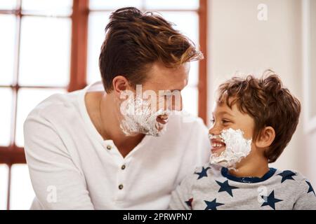 Spaß mit seiner ersten Rasur-Lektion. Ein Mann lehrt seinen kleinen Sohn, wie man zu Hause rasieren. Stockfoto