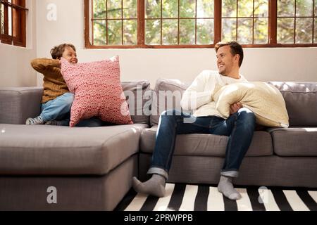 Beginnen Sie etwas. Ein Mann und sein kleiner Sohn, die einen Kissenkampf auf dem Sofa zu Hause haben. Stockfoto