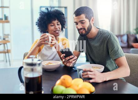 Es gibt einige gute Nachrichten über meinen Fußballverein. Ein junges Paar, das sich etwas auf einem Handy ansieht, während es zu Hause frühstückt. Stockfoto