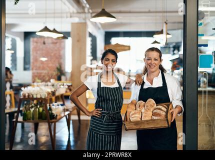 Niemand bekommt Brot wie wir. Zwei Frauen halten eine Auswahl an frisch gebackenen Broten in ihrer Bäckerei. Stockfoto