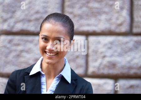 Sie meint Geschäfte. Ein Porträt einer schönen jungen Geschäftsfrau, die in der Stadt gegen eine Mauer steht. Stockfoto