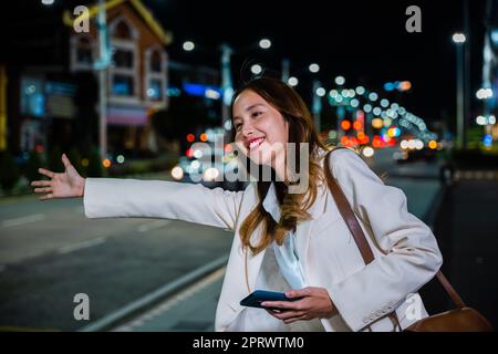 Eine Geschäftsfrau, die in der belebten Straße nachts mit einem Hageltaxi winkt, winkt Stockfoto