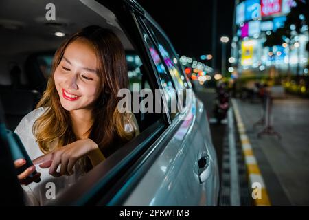 Asiatische Geschäftsfrau pendelt vom Büro in Taxi Rücksitz mit Handy auf der Straße Stockfoto