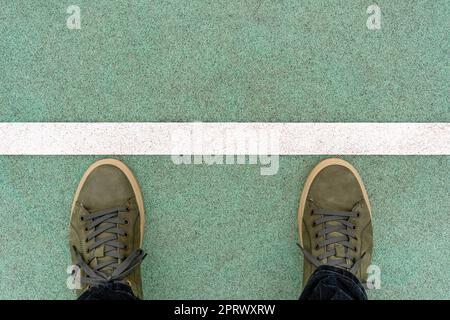 Männerfüße in grünen Lederschuhen stehen auf der gummierten Piste auf einer Startlinie Stockfoto