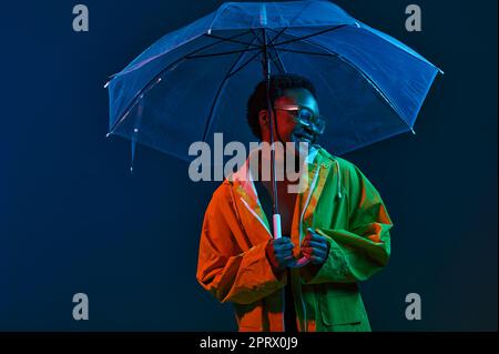 Hipster Frau im Regenmantel mit Regenschirm in Neonlicht Stockfoto