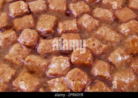 Braune Stücke in Gelee-Sauce mit nasser Hundefutter-Konsistenz aus der Nahaufnahme. Stockfoto