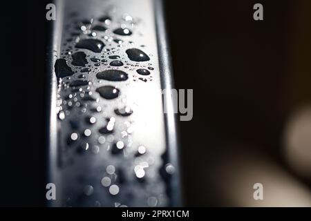 Wassertropfen abstrakt und mit unscharfem Hintergrund auf die Metalloberfläche eines Stuhls Stockfoto