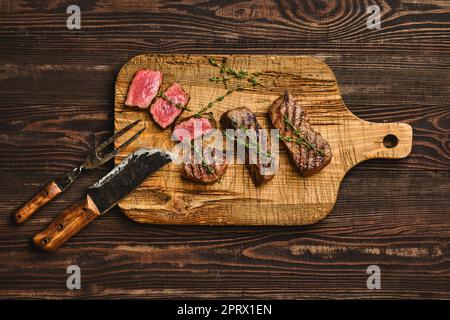 Blick von oben auf gegrilltes Rindersteak auf schäbigem Schneidebrett Stockfoto