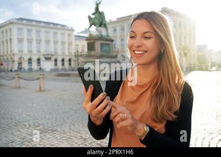 Schöne junge Frau auf dem Boulevard in der historischen Stadtlandschaft, in der Innenstadt, bei Sonnenuntergang, mit dem Smartphone Stockfoto