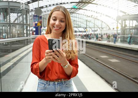 Lächelnd attraktiver brasilianischer Reisender kauft Ticket online mit Smartphone im Bahnhof. Speicherplatz kopieren. Stockfoto