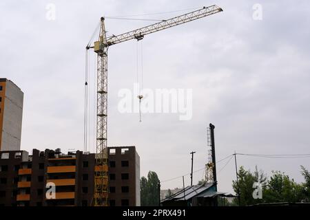 Ein Kran baut ein Haus in einer Höhe und hebt die Last in die obere Etage. Die Baustelle eines Wohngebäudes, ein Gebäude am Himmel. Hochwertiges Foto Stockfoto