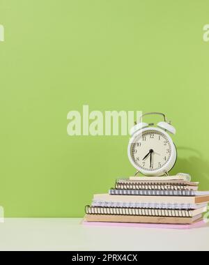 Rund-Wecker steht auf einem Stapel Notizbücher, grüner Hintergrund. Stockfoto