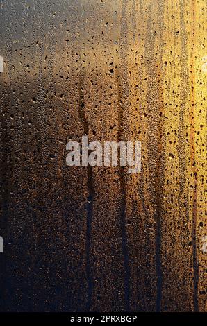 Die Textur von beschlagenem Glas mit vielen Tropfen und Kondensattropfen gegen das Sonnenlicht bei Sonnenaufgang. Hintergrundbild Stockfoto