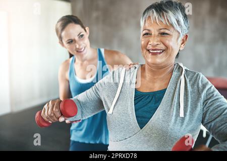 Fühlen Sie sich mit regelmäßigem Training in jedem Alter optimal. Eine ältere Frau, die mit Hilfe eines Physiotherapeuten Gewichte benutzt Stockfoto