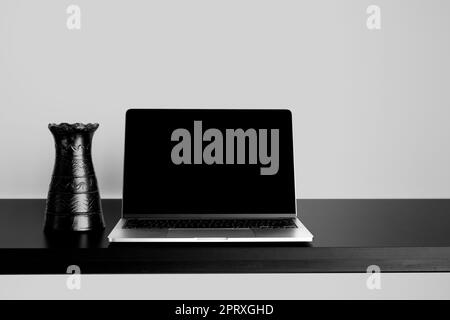 Laptop-Modell auf schwarzem Holztisch mit wechselbarem Desktophintergrund. Mit schwarzer Vase und grauem Hintergrund. Stockfoto