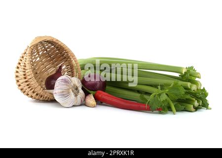 Rote und gelbe Zwiebeln fallen aus dem Korbkorb, rote Chilischote und Knoblauchzwiebeln vor frischem Sellerie-Stiel isoliert auf weißem Hintergrund Stockfoto