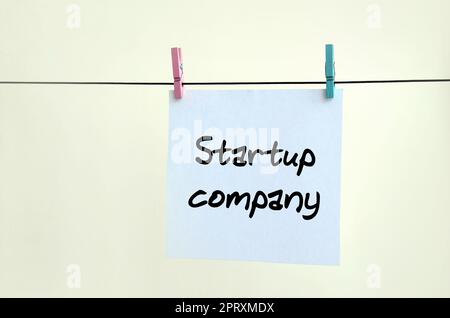 Startup-Unternehmen. Die Notiz ist auf einem weißen Aufkleber geschrieben, der mit einer Wäscheklammer an einem Seil auf einem beigen Hintergrund hängt Stockfoto