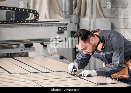 Holzwender messen und berechnen die richtige Größe des Werkstücks mit Hand- und Elektrowerkzeugen. Schneiden, Formen, Drehen, Glätten und Ausbalancieren von Holzbefestigungen Stockfoto