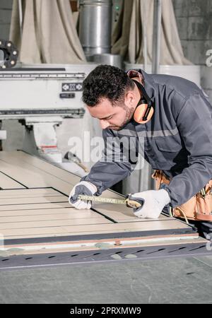 Holzwender messen und berechnen die richtige Größe des Werkstücks mit Hand- und Elektrowerkzeugen. Schneiden, Formen, Drehen, Glätten und Ausbalancieren von Holzbefestigungen Stockfoto