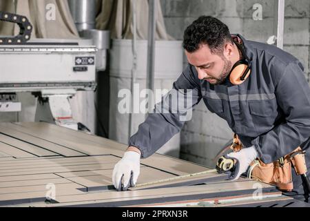 Holzwender messen und berechnen die richtige Größe des Werkstücks mit Hand- und Elektrowerkzeugen. Schneiden, Formen, Drehen, Glätten und Ausbalancieren von Holzbefestigungen Stockfoto