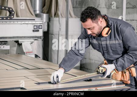 Holzwender messen und berechnen die richtige Größe des Werkstücks mit Hand- und Elektrowerkzeugen. Schneiden, Formen, Drehen, Glätten und Ausbalancieren von Holzbefestigungen Stockfoto